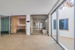 Spa interior with a wooden sauna on the left and glass doors, bright windows on the right.