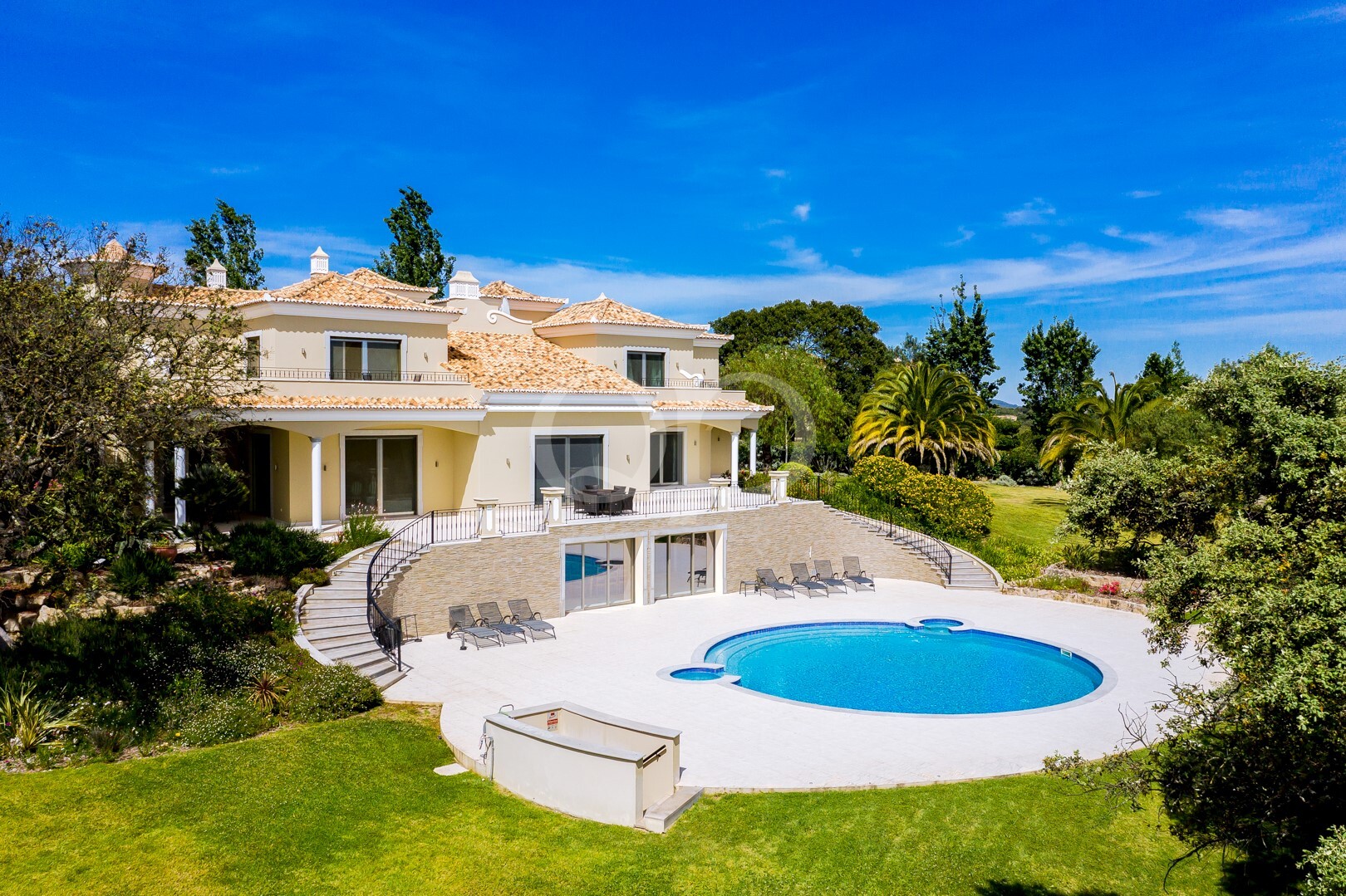 Villa de luxe aux murs en stuc blanc, aux tuiles en terre cuite et dotée d'une piscine bleue aux lignes courbes, située dans un jardin paysager.