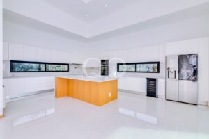 Modern white kitchen with glossy cabinets, marble countertops, and a warm wooden island at center.