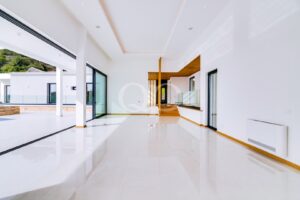 Bright open-plan living area with white walls, glossy floor, and large sliding glass doors to an outdoor patio.",