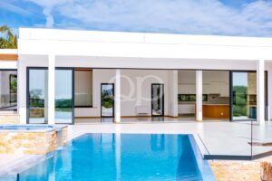Modern white house with large glass sliding doors opening to a blue swimming pool in the foreground.
