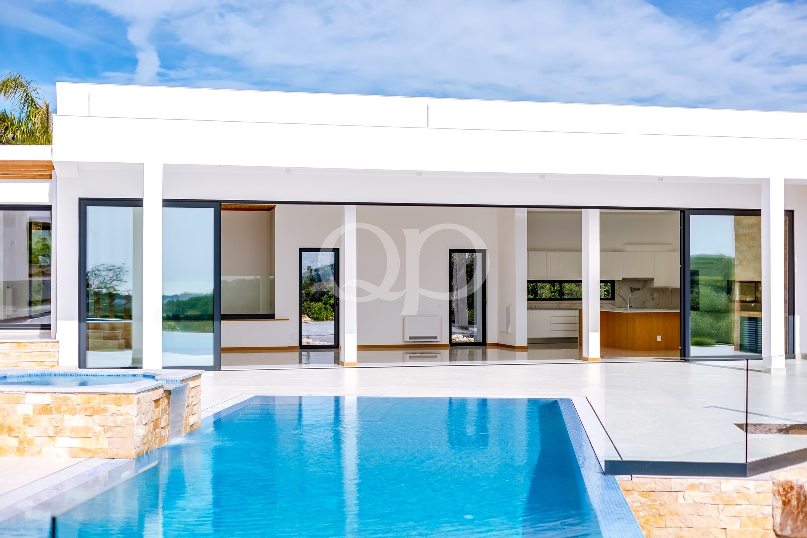 Modern white house with large glass sliding doors opening to a blue swimming pool in the foreground.
