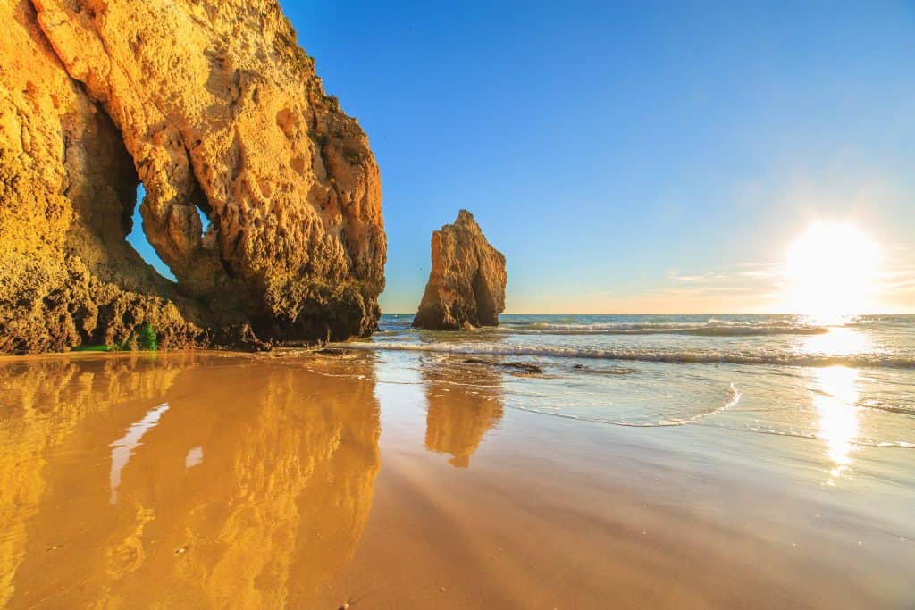 Golden sunset at Algarve beach with dramatic sea cliffs and rock formations reflecting in the water