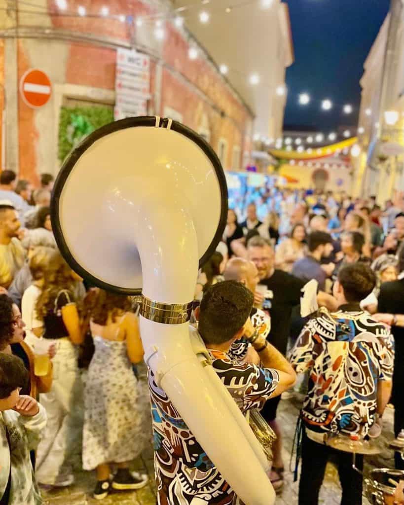 A lively street festival at night with musicians performing among a cheerful crowd under string lights.