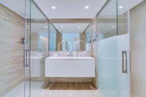 Modernes Badezimmer mit einer Duschkabine aus Glas, einem weißen Waschtisch und einem großen Spiegel, der einen klaren, hellen Raum widerspiegelt.