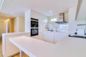 Helle, minimalistisch gestaltete Küche mit weißen Schränken, einem doppelten Einbaubackofen und einer Dunstabzugshaube aus Edelstahl über dem Kochfeld.