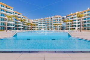 Eine Wohnanlage im Resort-Stil, die einen großen blauen Pool umgibt, mit Palmen und weißen Balkonen unter strahlend blauem Himmel.