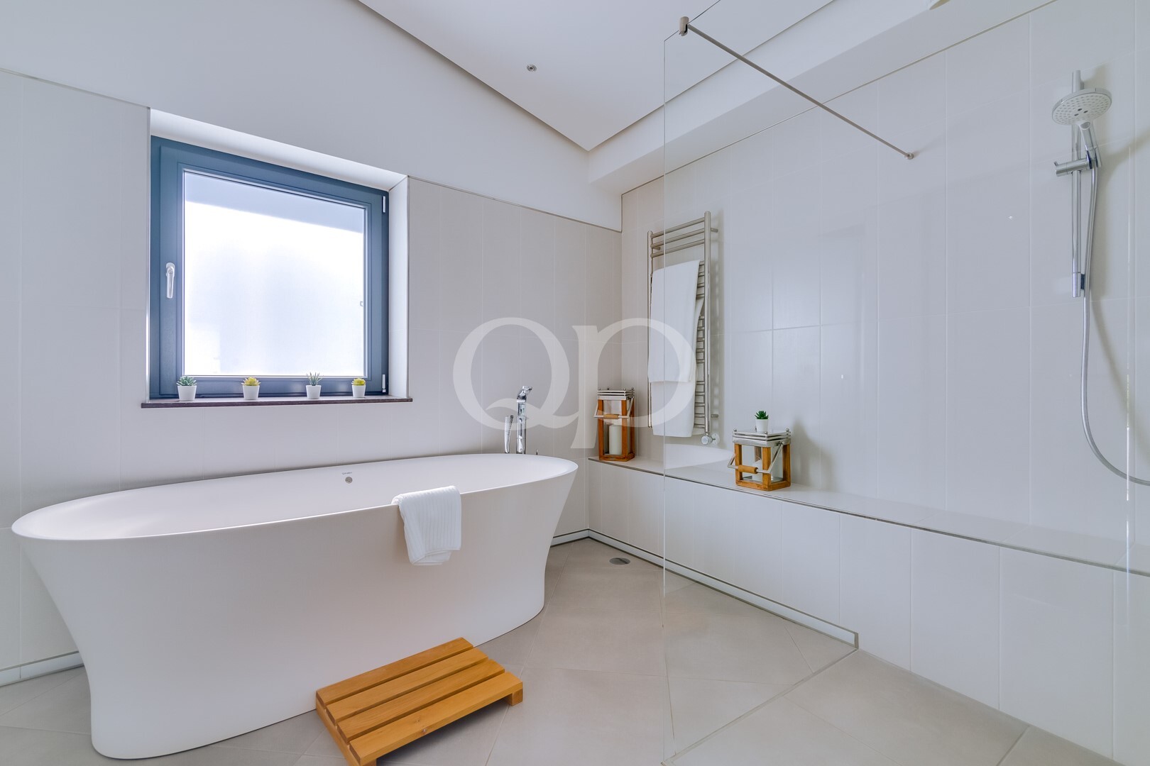 Modernes Badezimmer mit einer weißen freistehenden Badewanne neben einem Milchglasfenster und kleinen Topfpflanzen auf der Fensterbank