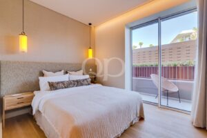 Bright modern hotel room featuring a king bed with white bedding, a padded headboard, and a balcony view through a sliding glass door.