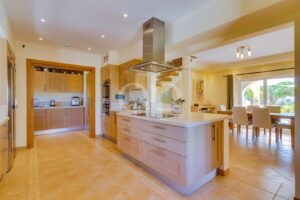 Bright open-plan kitchen with an island, stainless range hood, and adjacent dining area overlooking a garden.