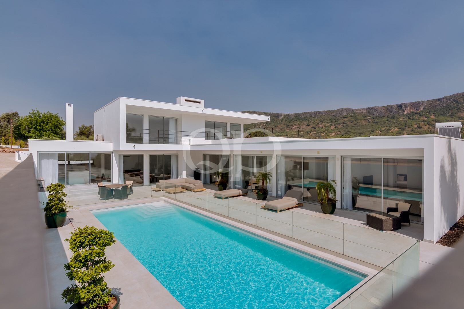 Moderne weiße Villa mit einem rechteckigen Pool, einer Poolumzäunung aus Glas und einem Loungebereich am Pool.