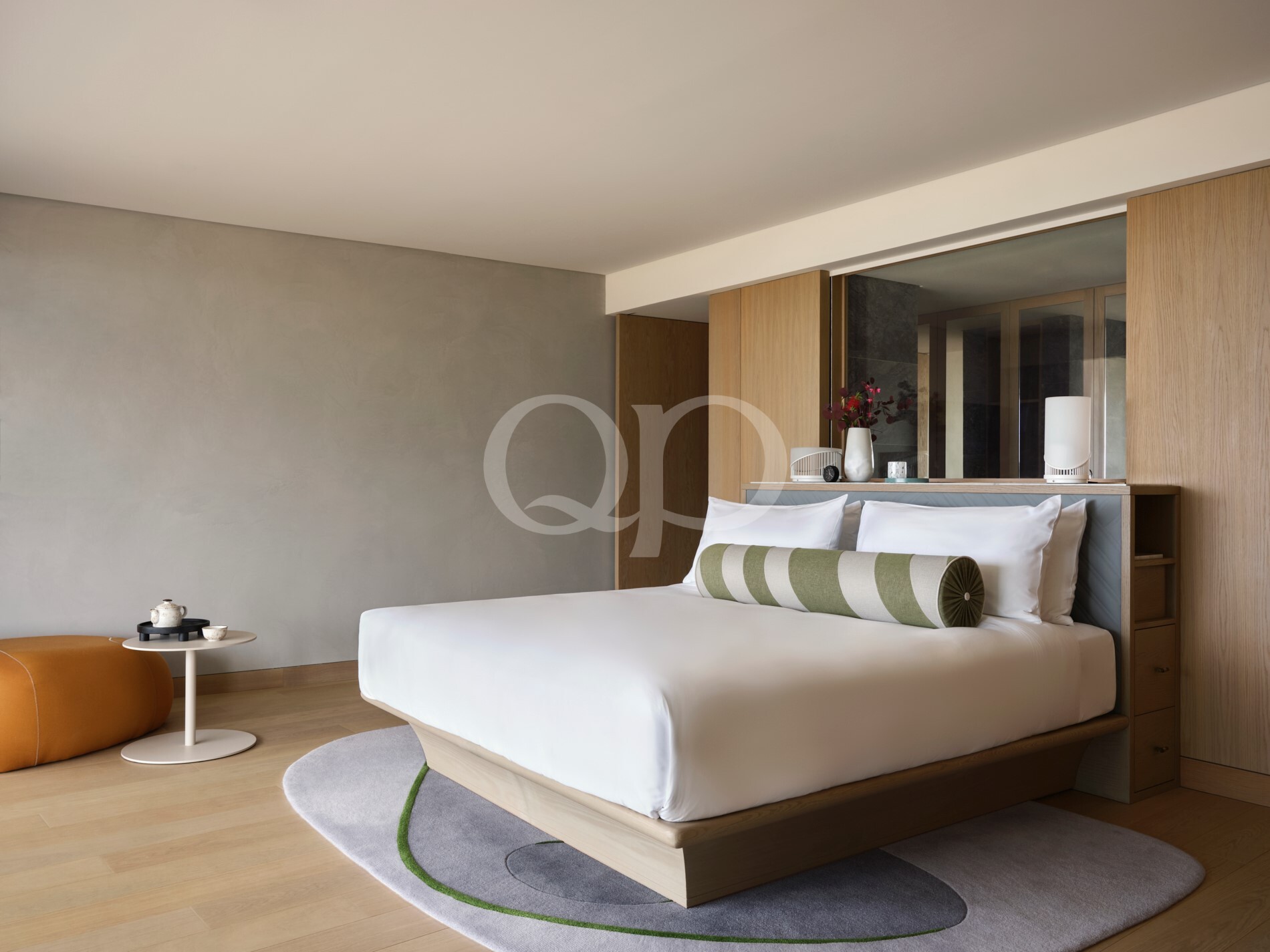 Modern hotel bedroom with white bedding, grey wall, and light wood headboard and cabinetry.