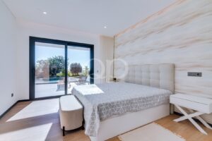 Bright modern bedroom with a tufted beige headboard, gray geometric bedspread, and sliding glass doors to an outdoor patio and pool.
