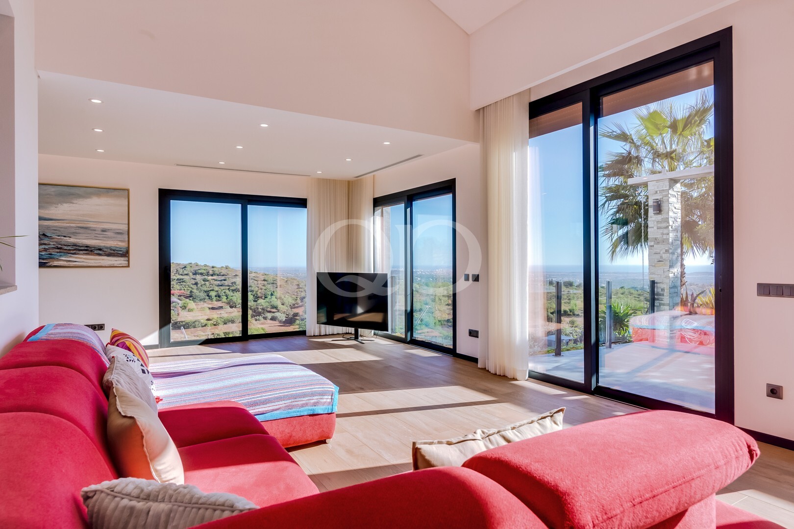 Bright living room with a red sectional sofa and large glass doors showing a panoramic outdoor landscape with palm trees.