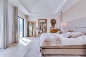 Une chambre lumineuse, digne d'un hôtel, avec un grand lit beige, une tête de lit rembourrée et une décoration aux tons neutres.