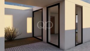 Extérieur d'une maison moderne de couleur beige, avec de grandes portes vitrées, une terrasse en bois et un arbuste du désert au premier plan, au coucher du soleil.