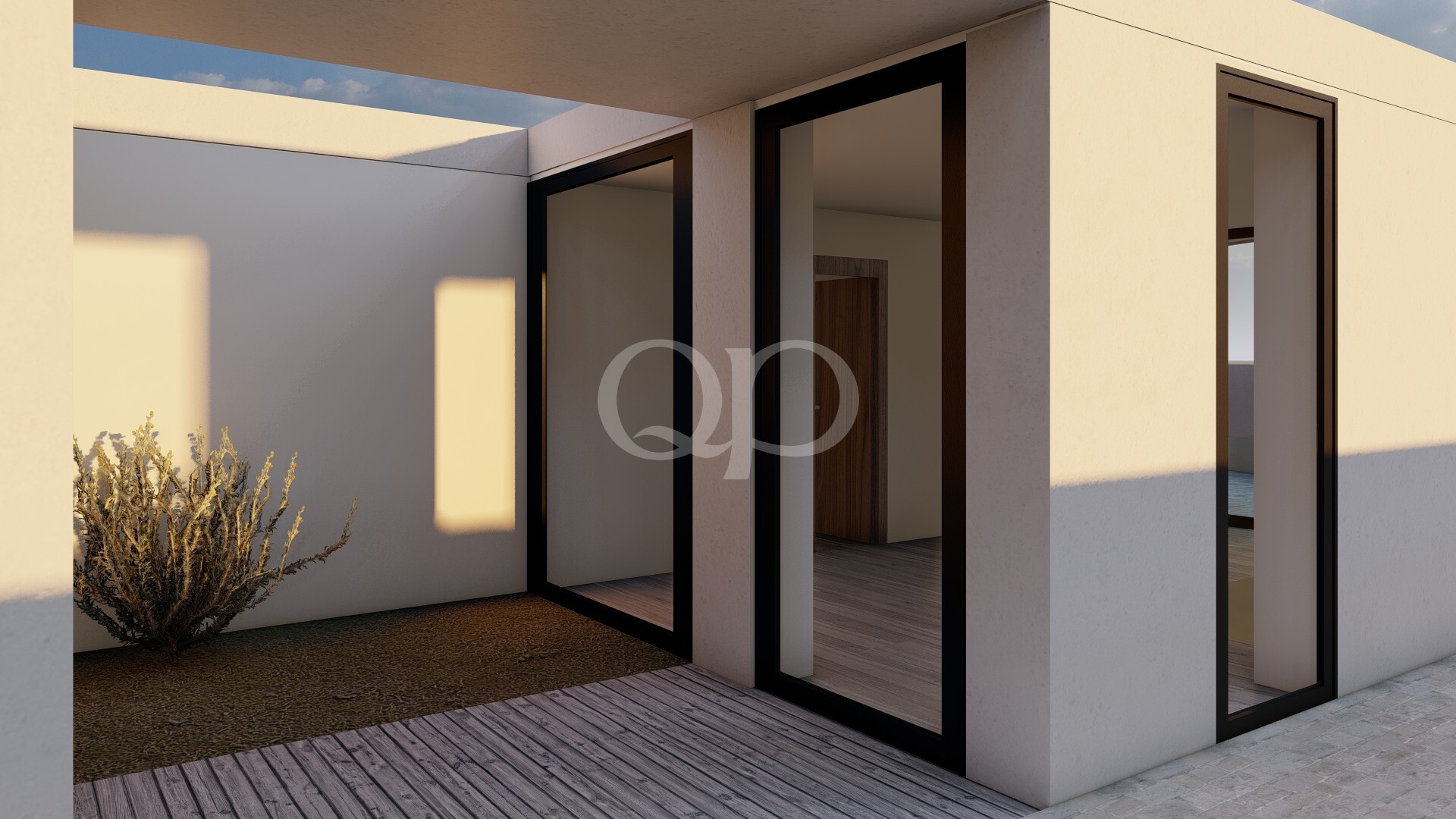 Extérieur d'une maison moderne de couleur beige, avec de grandes portes vitrées, une terrasse en bois et un arbuste du désert au premier plan, au coucher du soleil.