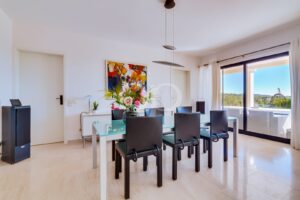Bright dining room with glass table, six black chairs, and a large colorful painting on the wall.