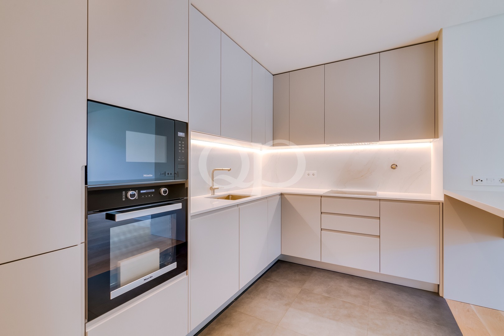 Moderne L-förmige Küche mit mattbeigen Schränken, eingebauter Mikrowelle und Backofen sowie LED-Beleuchtung unter den Schränken.