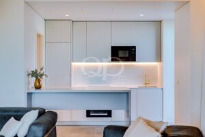 Moderne weiße Küche mit grauen Schränken, eingebauter Mikrowelle und warmer Unterbauleuchte entlang einer Marmor-Rückwand.
