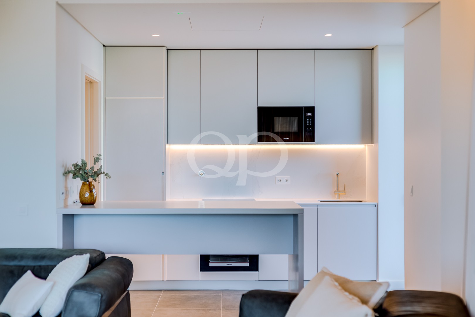 Moderne weiße Küche mit grauen Schränken, eingebauter Mikrowelle und warmer Unterbauleuchte entlang einer Marmor-Rückwand.