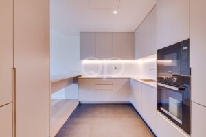 Minimalist L-shaped kitchen with pale gray cabinets, under-cabinet lighting, and built-in oven/microwave on the right side.