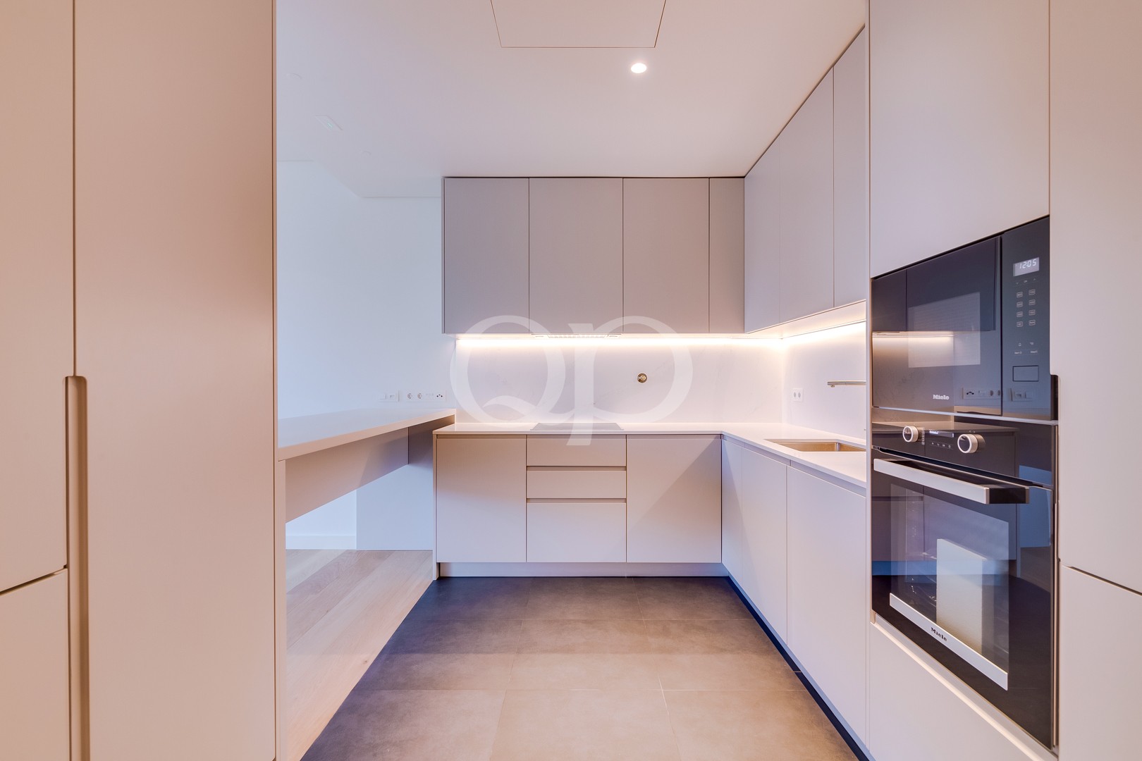 Minimalist L-shaped kitchen with pale gray cabinets, under-cabinet lighting, and built-in oven/microwave on the right side.