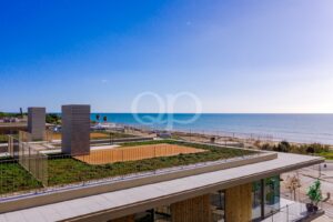 Seaside modern terrace with metal railings, rooftop greenery, and a calm blue sea under a clear sky in the background.
