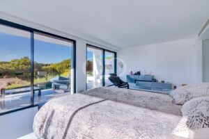 Chambre lumineuse et moderne dotée de grandes baies vitrées donnant sur un balcon et un paysage verdoyant ; couette à motif peau de serpent sur le lit situé à droite.