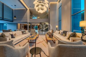 Sala de estar luxuosa em plano aberto, com sofás seccionais em bege, almofadas coloridas e um grande lustre escultural.
