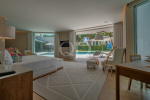 Suíte de hotel de luxo com uma cama king size, área de estar e portas de vidro que dão acesso a uma área ajardinada ao ar livre, com vista para a piscina.
