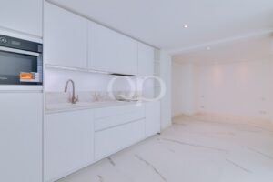 Modern white kitchen with built-in stainless steel oven, glossy cabinets, marble backsplash, and a curved faucet over a white sink.