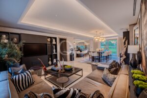 Ein großzügiger, offener Wohnbereich mit beigen Sofas, Kissen im Zebramuster und einem schwarzen Couchtisch, der in einen Essbereich und zu großen Fenstern mit Blick ins Freie übergeht.