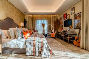 Gemütliches Hotelzimmer mit zwei Betten, gemusterten Steppdecken und beigen Vorhängen; warme Beleuchtung und eine Bilderwand auf der rechten Seite.