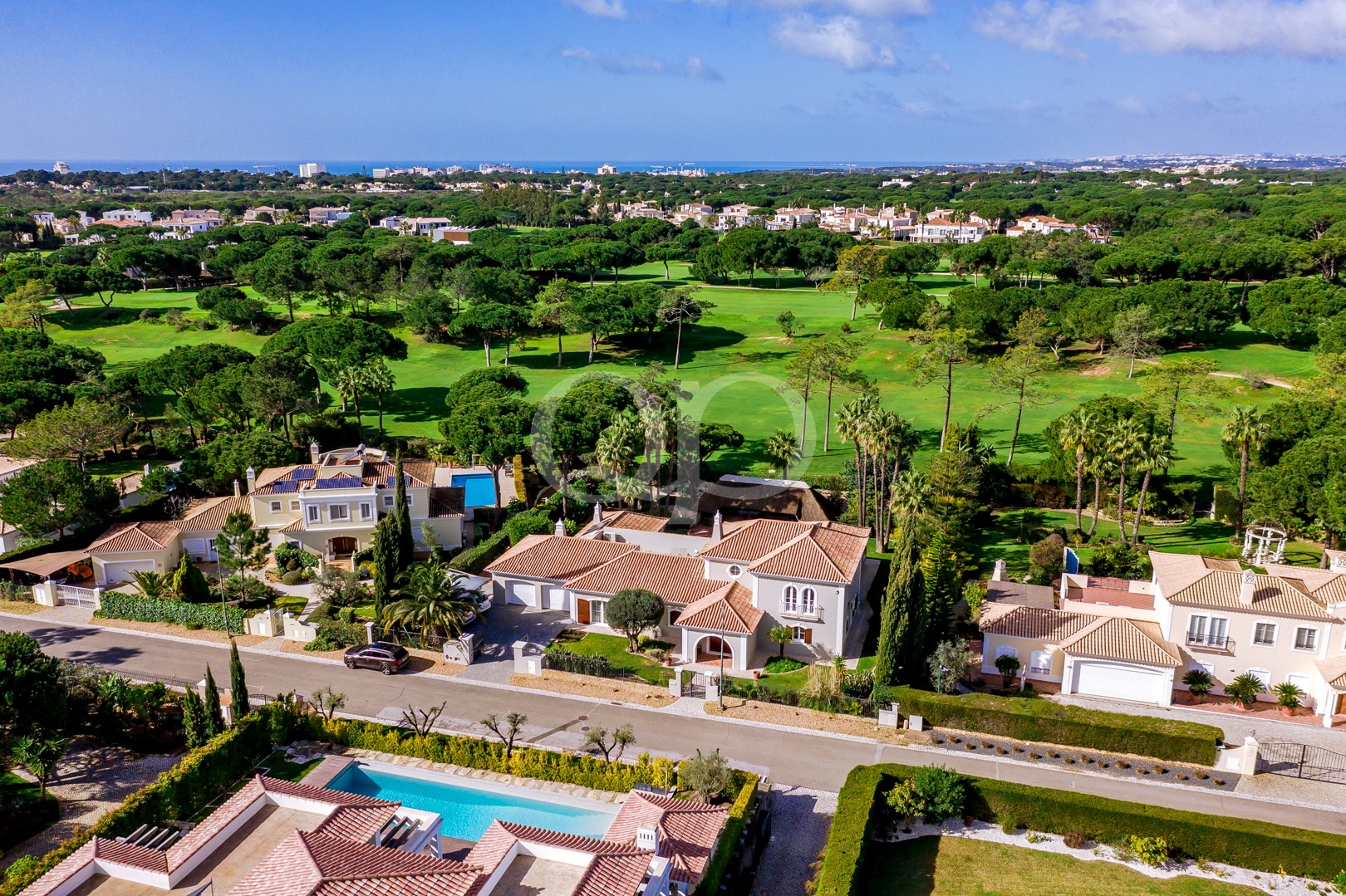Vue aérienne d'un lotissement fermé composé de maisons de style méditerranéen alignées le long d'une rue, à proximité d'un grand parcours de golf verdoyant et d'arbres.