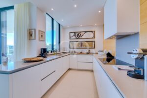 Bright white L-shaped kitchen with large windows, built-in cabinets, and modern appliances.