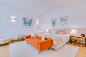 Bright hotel-style bedroom with a white bed, an orange sofa, and framed artwork by the wall lampside.