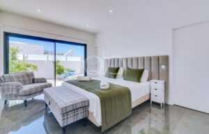 Bright modern bedroom with a large sliding glass door to a sunny patio, a king bed with green accents, and a plaid ottoman.