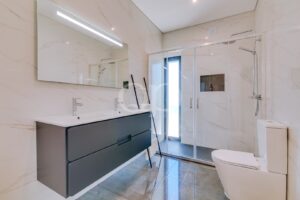 Salle de bains moderne équipée d'un meuble-lavabo suspendu à double vasque de couleur foncée et d'un grand miroir mural doté d'une bande lumineuse LED