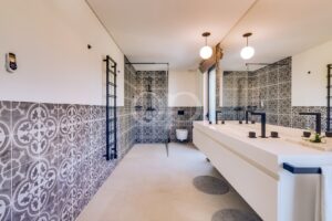Salle de bains moderne avec des équipements noirs audacieux, du carrelage gris à motifs et un double lavabo blanc dont le reflet se dégage dans un grand miroir.