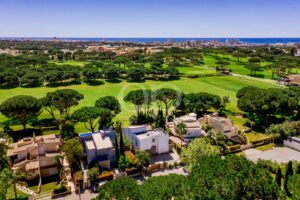 Aerial view of a coastal city with a large green golf course and residential neighborhood in the foreground, ocean on the horizon.