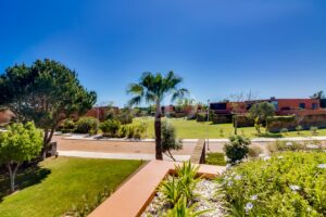 Sunny campus scene with palm trees, green lawns, and low, orange-walled buildings against a clear blue sky.