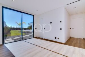 Quarto luminoso e moderno, com grandes portas de vidro do chão ao teto que se abrem para um jardim ajardinado com palmeiras no exterior.