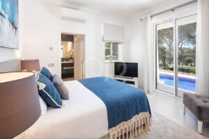 Bright hotel bedroom with a white and blue bed, blue throw, bedside lamps, and a sliding glass door to the pool outside.