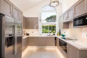 Bright modern kitchen with gray cabinets, stainless steel refrigerator, and a large arched window overlooking a garden outside.