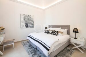 Bright, minimalist bedroom with a gray upholstered bed, white bedding, and black-and-white decorative pillows.
