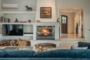 Living room with a lit fireplace at center, flanked by a mantel, shelves with books, and decorative statues.
