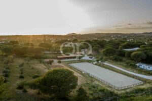 Aerial view of a rural landscape at sunset with trees, fences, and scattered houses across rolling hills.