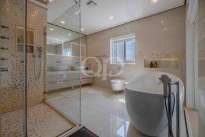 Modern bathroom with a glass-enclosed shower, white fixtures, and gold mosaic tiles on the walls and floor.