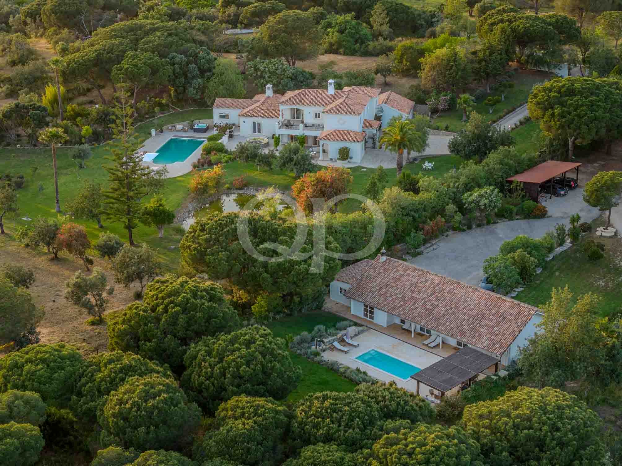 Aerial view of a white house with red-tiled roof, a rectangular blue pool, and surrounding green lawn and trees.